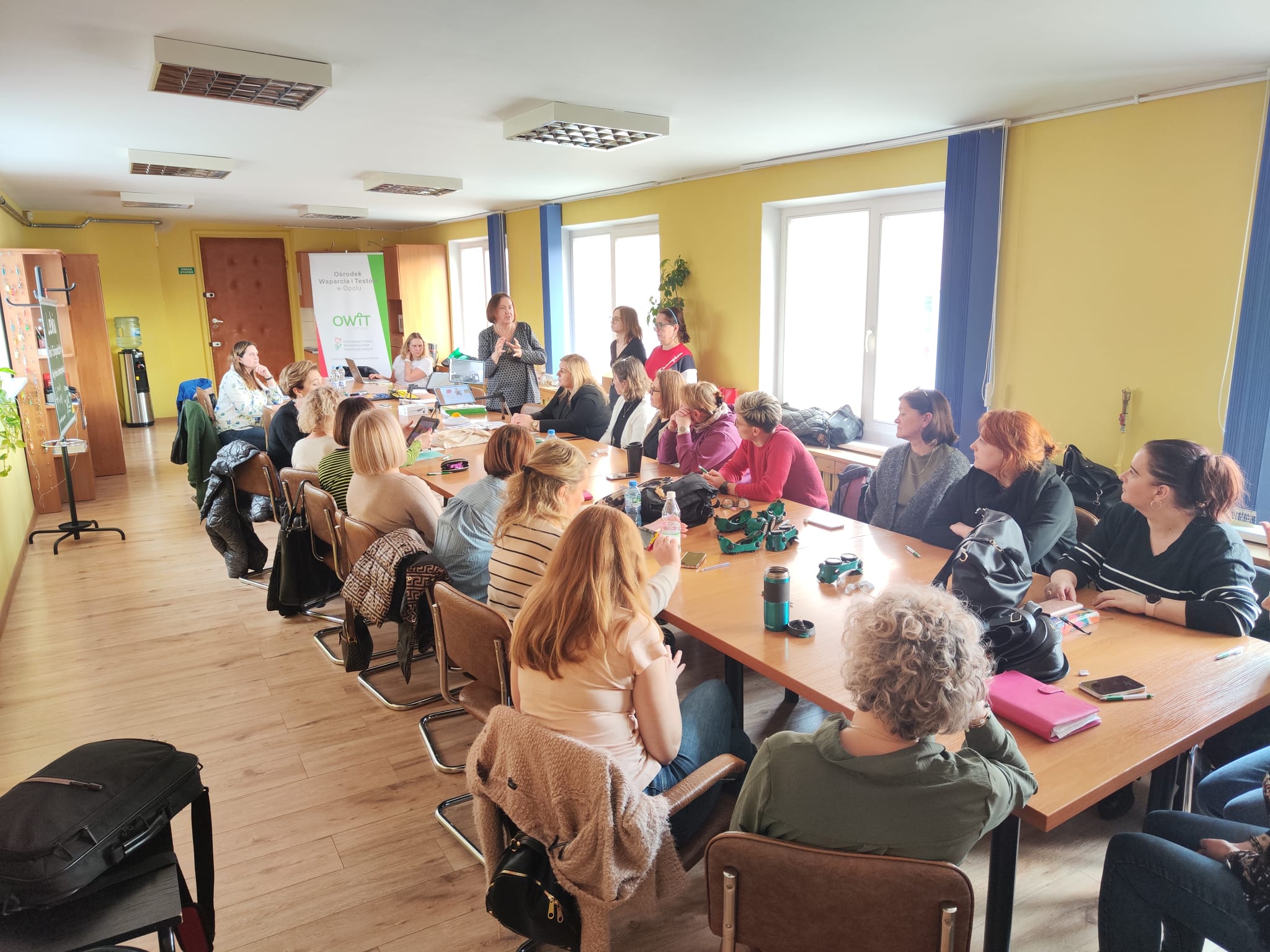 Przy długim stole siedzi ponad 20 kobiet. To kadra pedagogiczna szkoły podstawowej w Lewinie Brzeskim. W głębi stoi pracownica OWiT i opowiada o technologiach asystujących