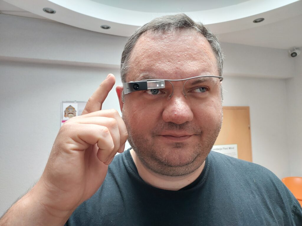 Testujemy Envision: głowa mężczyzny, który ma założone okulary Envision. Palcem wskazującym prawej ręki ustawia funkcje okularów.